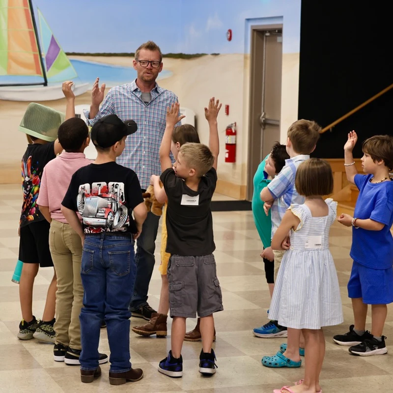 A children's ministry leader teaches a group of kids with hands raised at The Crossing in Milton, DE.